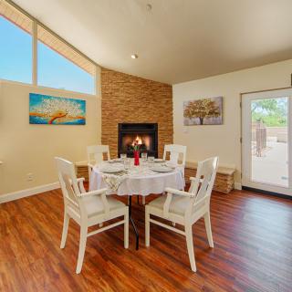 A cozy dining room with a round table set for four, featuring a warm fireplace and bright natural lighting.
