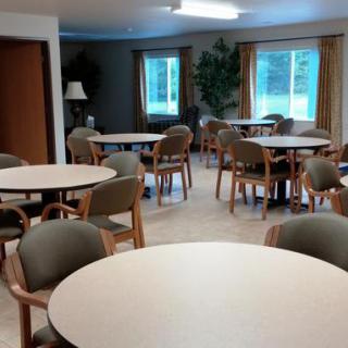 A spacious room with round tables and chairs, featuring large windows and potted plants.
