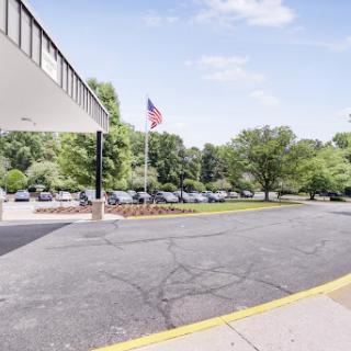 A view of the hotel entrance with an American flag and a landscaped parking area.