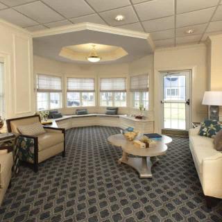 A cozy living room with comfortable seating, a patterned carpet, and large windows providing ample natural light.