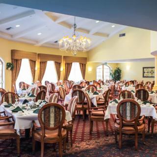 An elegantly decorated dining room with neatly arranged tables and chairs, featuring a chandelier and large windows.