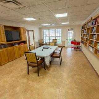 A spacious meeting room featuring a large table surrounded by chairs, shelves filled with books, and a television on the wall.