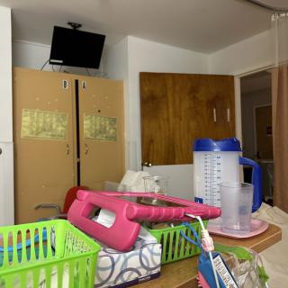 A hospital room with cabinets, TV, and medical supplies on a tray.
