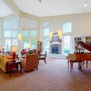 A spacious and elegant living room with a high ceiling, featuring a grand piano, large windows, and a cozy fireplace.