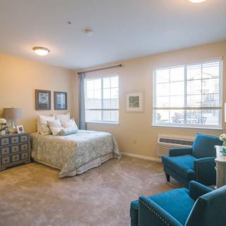 A cozy bedroom with a neatly made bed, turquoise armchairs, and soft lighting.
