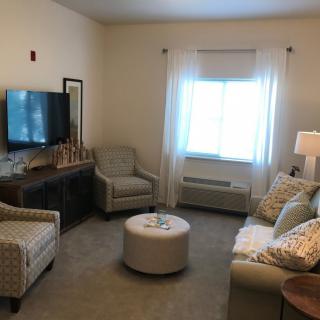 A cozy living room with a television, sofa, chairs, and a coffee table.