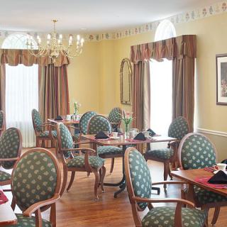 A formal dining room with elegant furniture and large windows adorned with curtains.