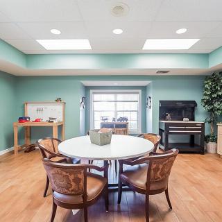 A cozy dining room with a round table and chairs, featuring a piano and soft lighting.