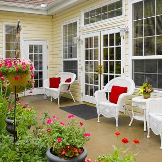 A cozy patio with white chairs and a table, surrounded by vibrant flowers.