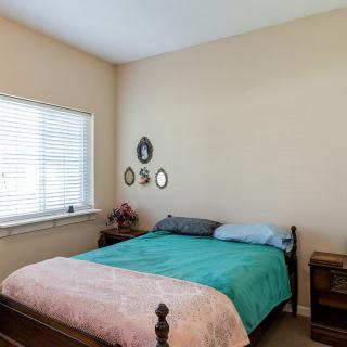 A cozy bedroom featuring a bed with colorful bedding, a window with blinds, and decorative wall art.