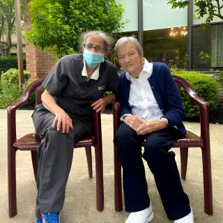 Two elderly individuals sitting outside together, with one wearing a mask.