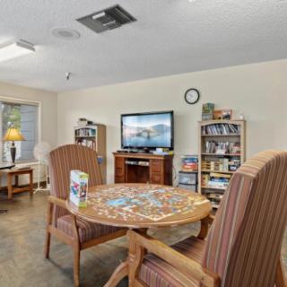 A cozy living room features a table with a puzzle, comfortable chairs, bookshelves, and a television.