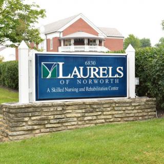 A sign for 'The Laurels of Norworth', a skilled nursing and rehabilitation center, set in front of a brick building.