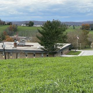 A serene view of a building surrounded by lush green grass and rolling hills under a cloudy sky.