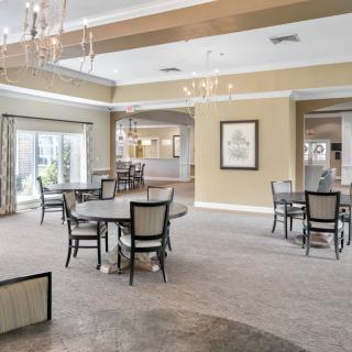 A spacious and elegantly designed dining area with multiple tables and chairs, featuring chandeliers and large windows.