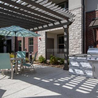 A sunny patio area with a pergola, outdoor seating, and a grill.