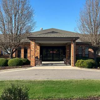 A brick building with an entrance, surrounded by trees and bushes under a clear blue sky.