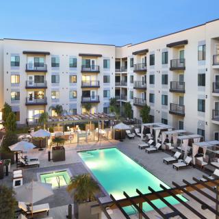 Modern apartment complex with a central swimming pool and outdoor seating area during the evening.