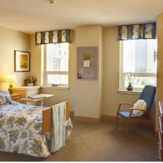 A cozy hospital room with a single bed, chair, and two windows providing natural light.