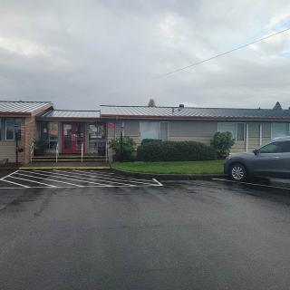 A single-story building with a car parked in an adjacent parking lot on a cloudy day.