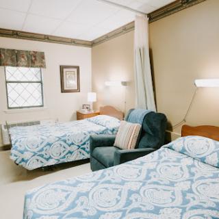 A cozy hotel room featuring two neatly made beds, a comfortable armchair, and warm lighting.
