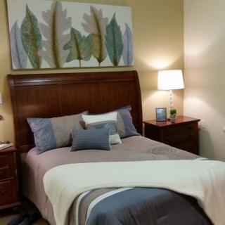 A cozy bedroom with a wooden bed frame, decorated with pillows and a blanket, alongside two bedside tables with lamps and artwork above the headboard.