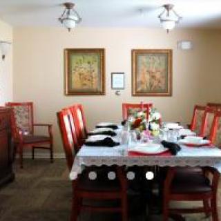 A dining room with a table set for a meal, featuring elegant chairs, artwork on the walls, and decorative lighting.