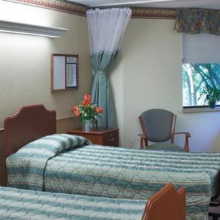 A hospital room with two neatly made beds and a chair by the window.