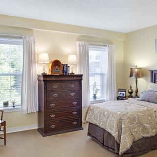 A cozy bedroom with a bed, dresser, and two windows adorned with curtains.