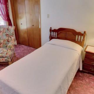 A cozy bedroom featuring a single bed with a wooden headboard, an upholstered chair, and a nightstand beside it.