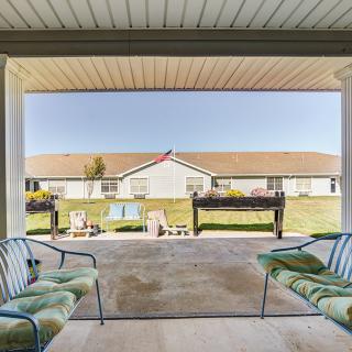 A cozy patio with cushioned chairs overlooks a sunny yard and neighboring building.