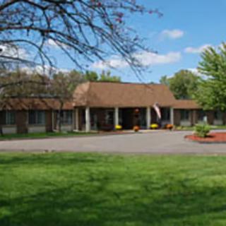 A single-story building surrounded by a lush green lawn and trees under a clear blue sky.