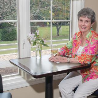 A woman enjoying a drink at a cafe table, surrounded by natural light and flowers.
