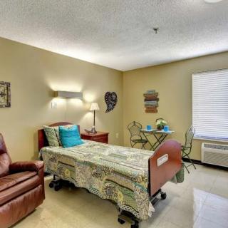 A neatly arranged room with a hospital bed, recliner, and small dining area by the window.