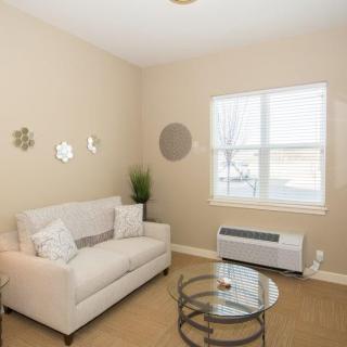 A cozy living room with a beige sofa and glass coffee table, complemented by wall decor and an indoor plant near the window.