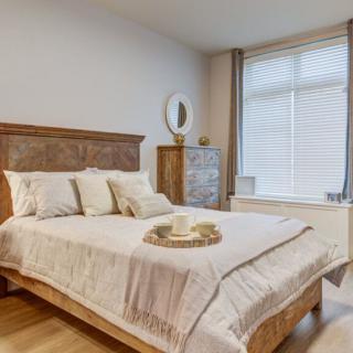 A cozy bedroom featuring a wooden bed frame, soft cushions, and natural lighting from a large window.