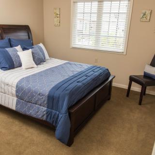 A neatly arranged bedroom with a bed, blue bedding, and a chair near the window.
