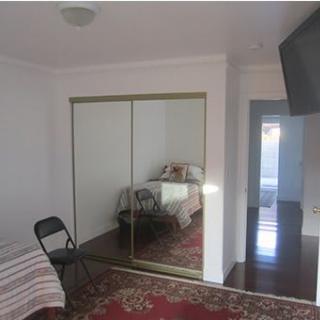 A tidy bedroom with a bed, mirrored closet, chair, and wall-mounted TV.
