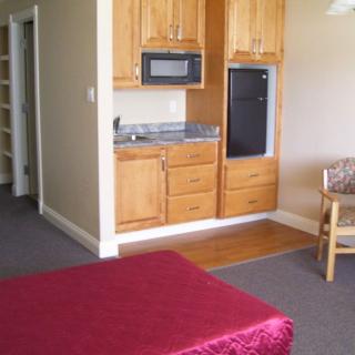 A cozy hotel room featuring a kitchenette with wooden cabinets, microwave, and refrigerator.