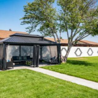 A backyard featuring a black gazebo with outdoor seating, surrounded by a lush green lawn and trees.