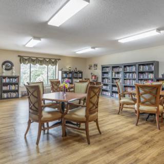 A spacious library room with wooden tables and chairs, lined with bookshelves full of books.