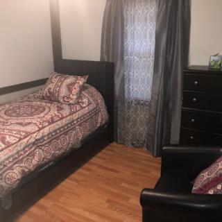 A cozy bedroom with a single bed, dresser, and curtains on a wooden floor.