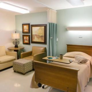 A well-furnished hospital room with a bed, seating area, and medical equipment.