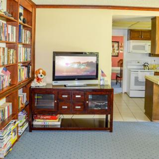 A cozy living room with a bookshelf, television, and a view into the kitchen.