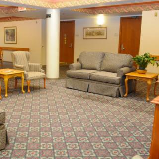 A cozy lobby area featuring a sofa set, chairs, wooden tables, and patterned carpeting.