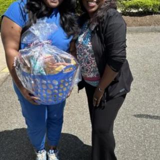 Two people smiling outdoors, holding a gift basket.
