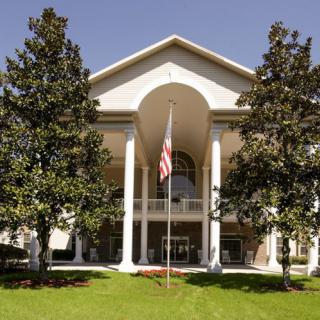 A grand building with large columns and an American flag at the entrance, surrounded by trees.