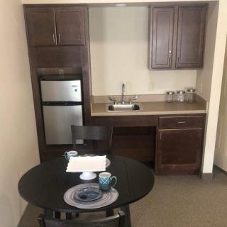 A compact kitchen with a small table and chairs, featuring a refrigerator, sink, and cabinets.