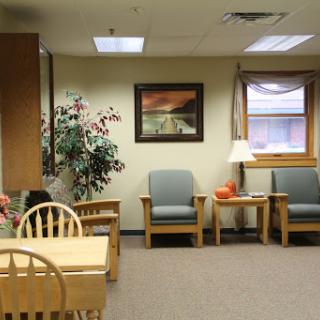 A cozy waiting area featuring comfortable seating and a small table, complemented by indoor plants.