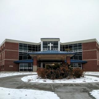 A modern church building with a prominent cross, surrounded by snow on a winter day.
